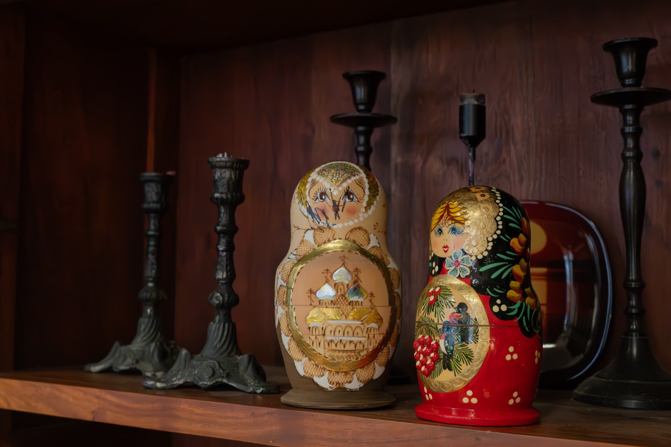 Kaksi maalaettua venäläistä matryoshka-nukkea puisella hyllyllä, taustalla mustia kynttilänjalkoja.