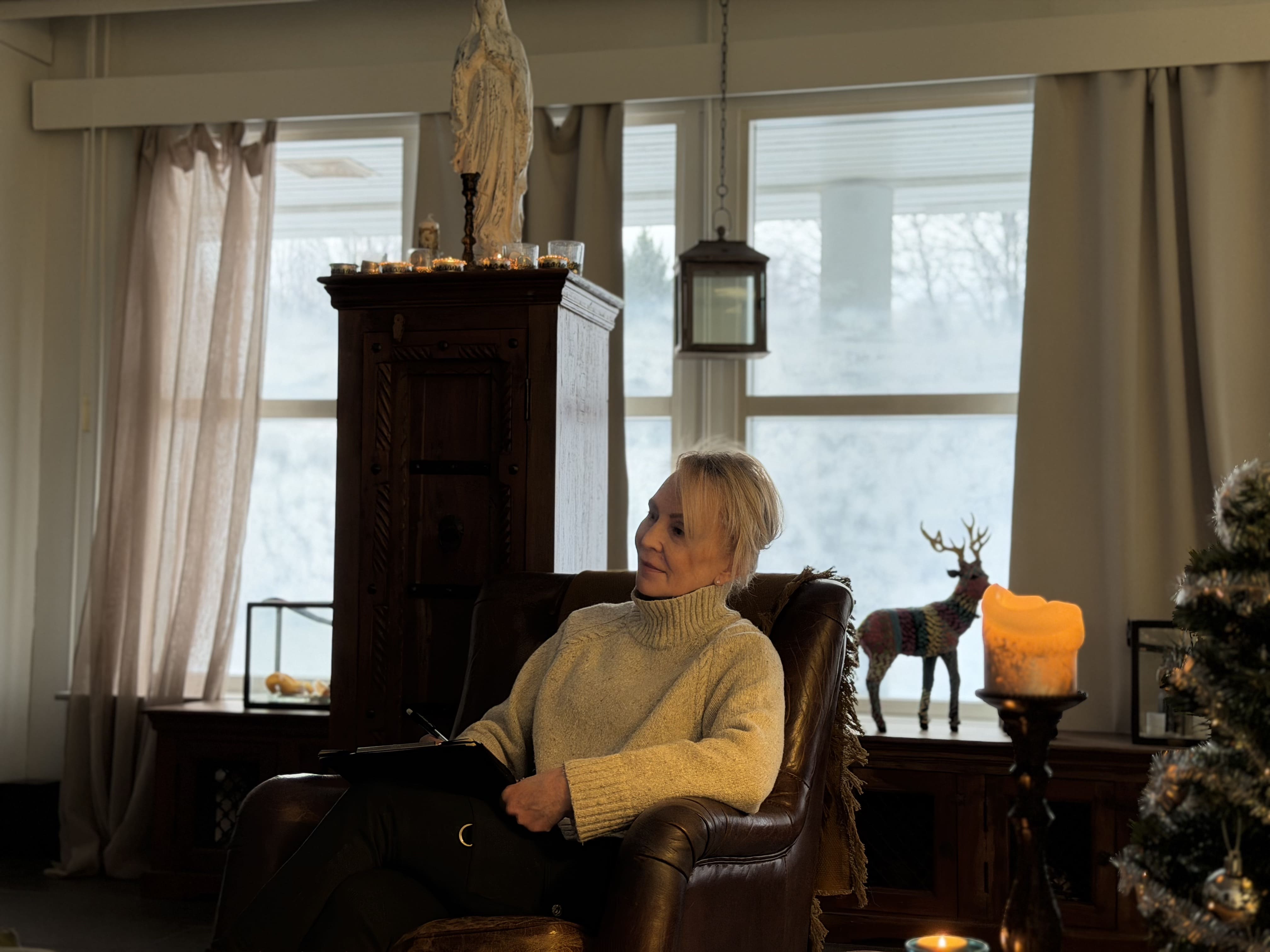 Nainen istuu nahkatuolissa kodikkaassa huoneessa, jossa on joulukoristeita ja kynttilöitä.