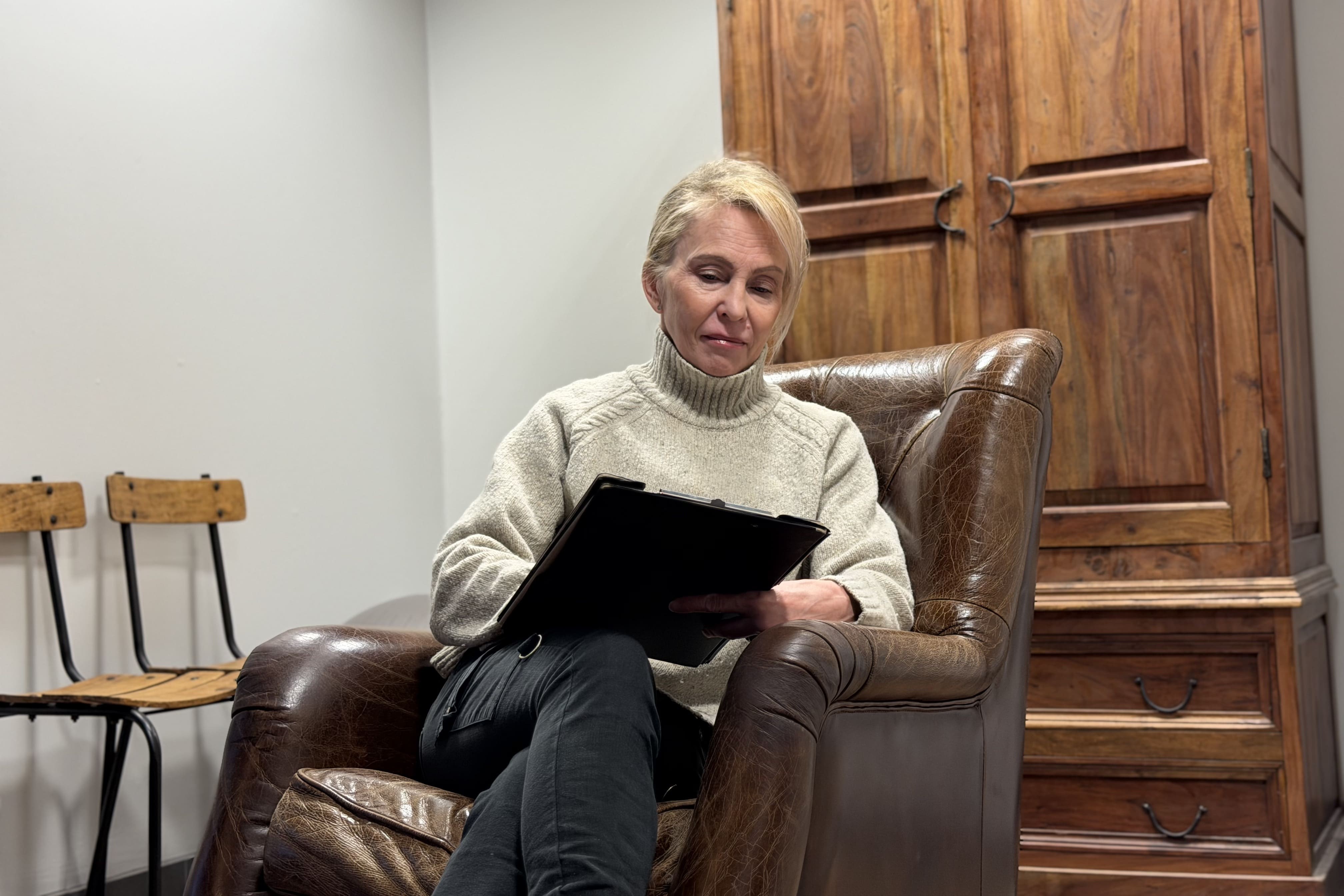 Aikuinen nainen istuu ruskeassa nahkatuolissa kirjoittaen mustaan lehtiöön.