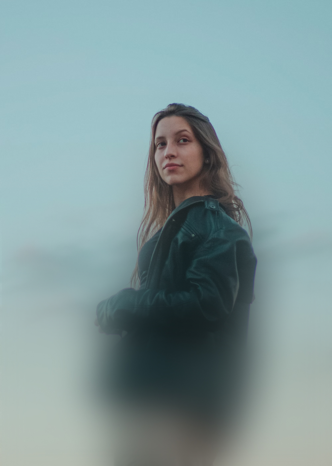 Nuori nainen mustassa takissa katsomassa sivulle sinistä taivasta vasten.