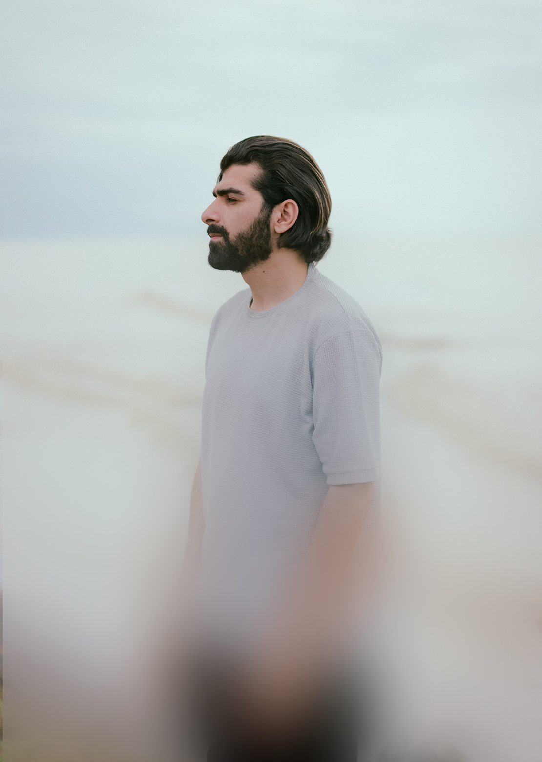 Mies vaaleansinisessä paidassa katselemassa vasemmalle, taustalla hämärä ranta.